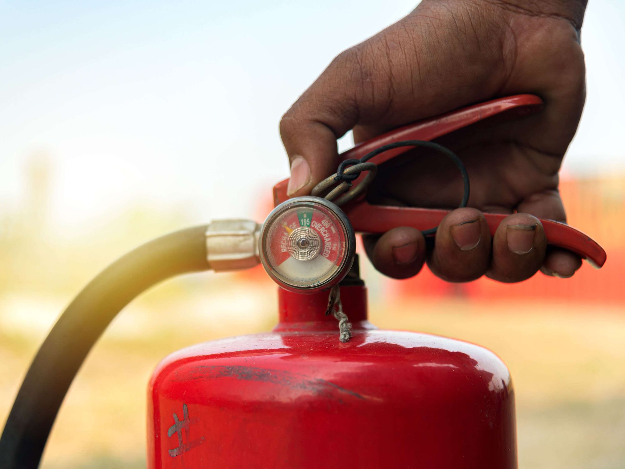 A closeup of a hand on the handle of a red fire extinguisher.