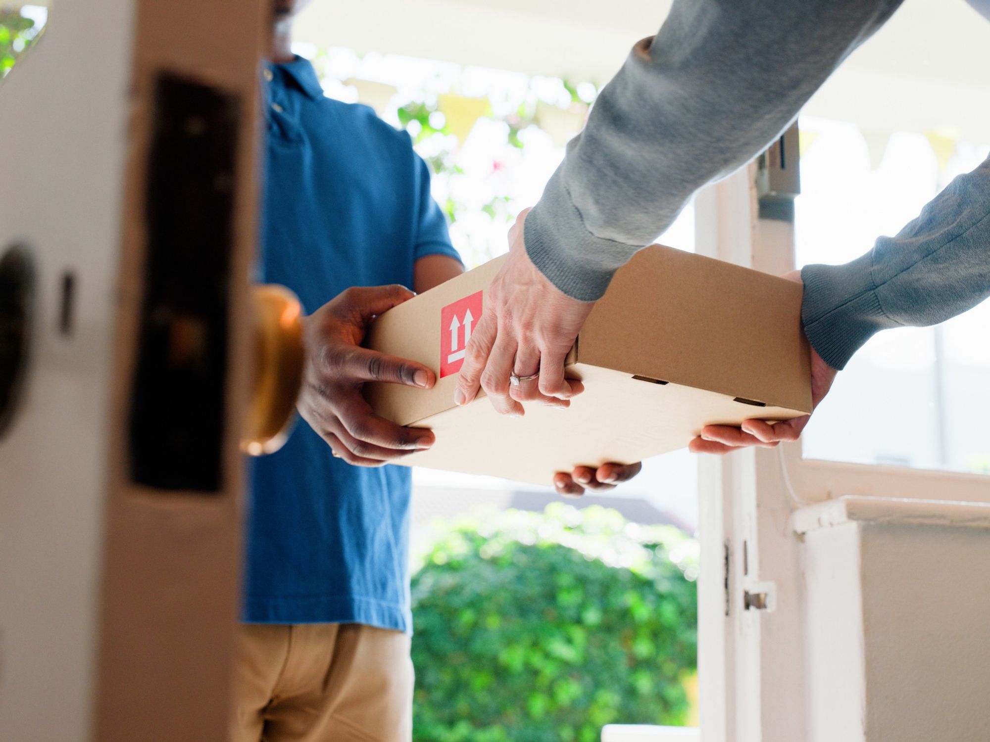 A delivery driver hands over a package to a customer in a doorway.