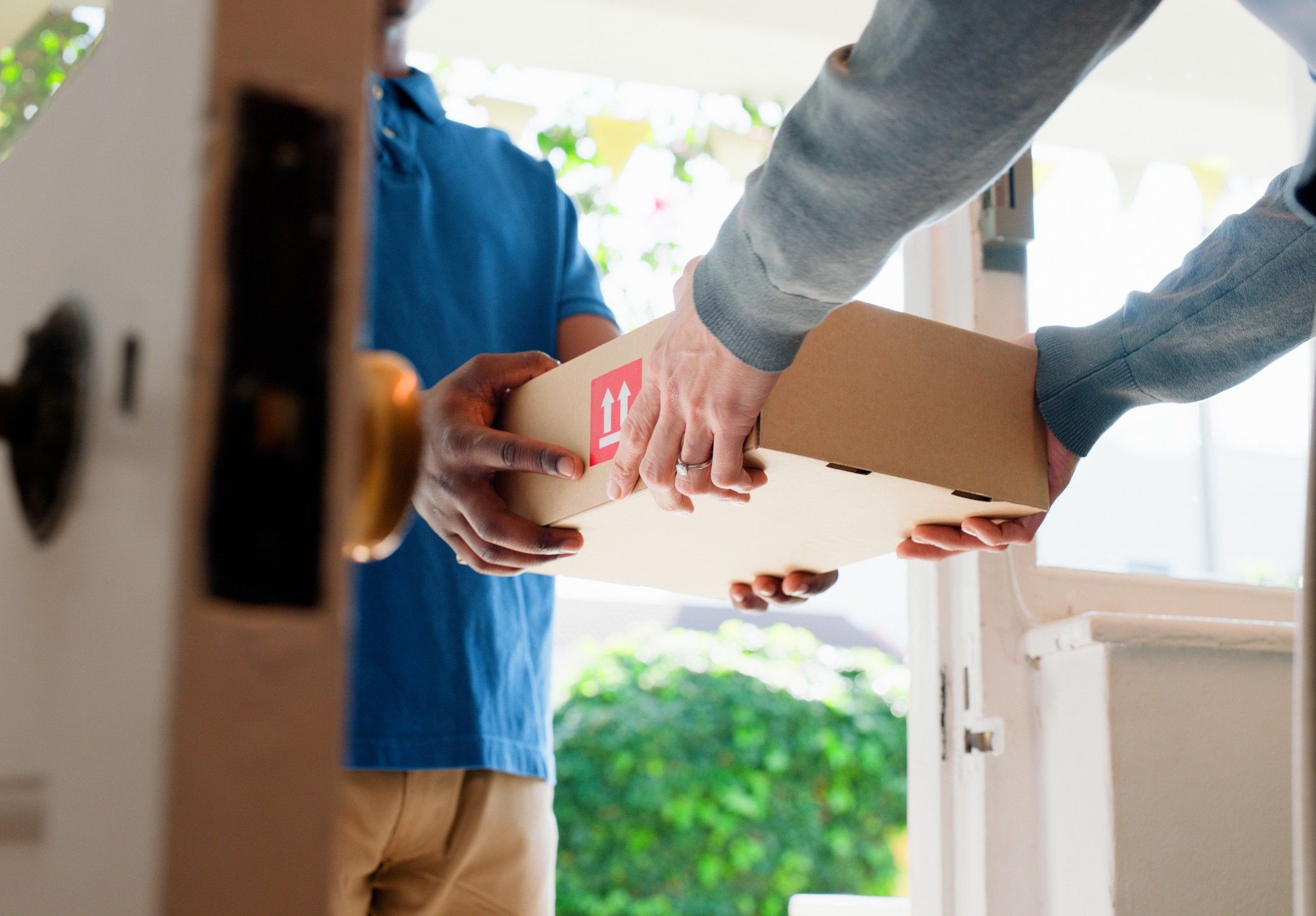 A delivery driver hands over a package to a customer in a doorway.