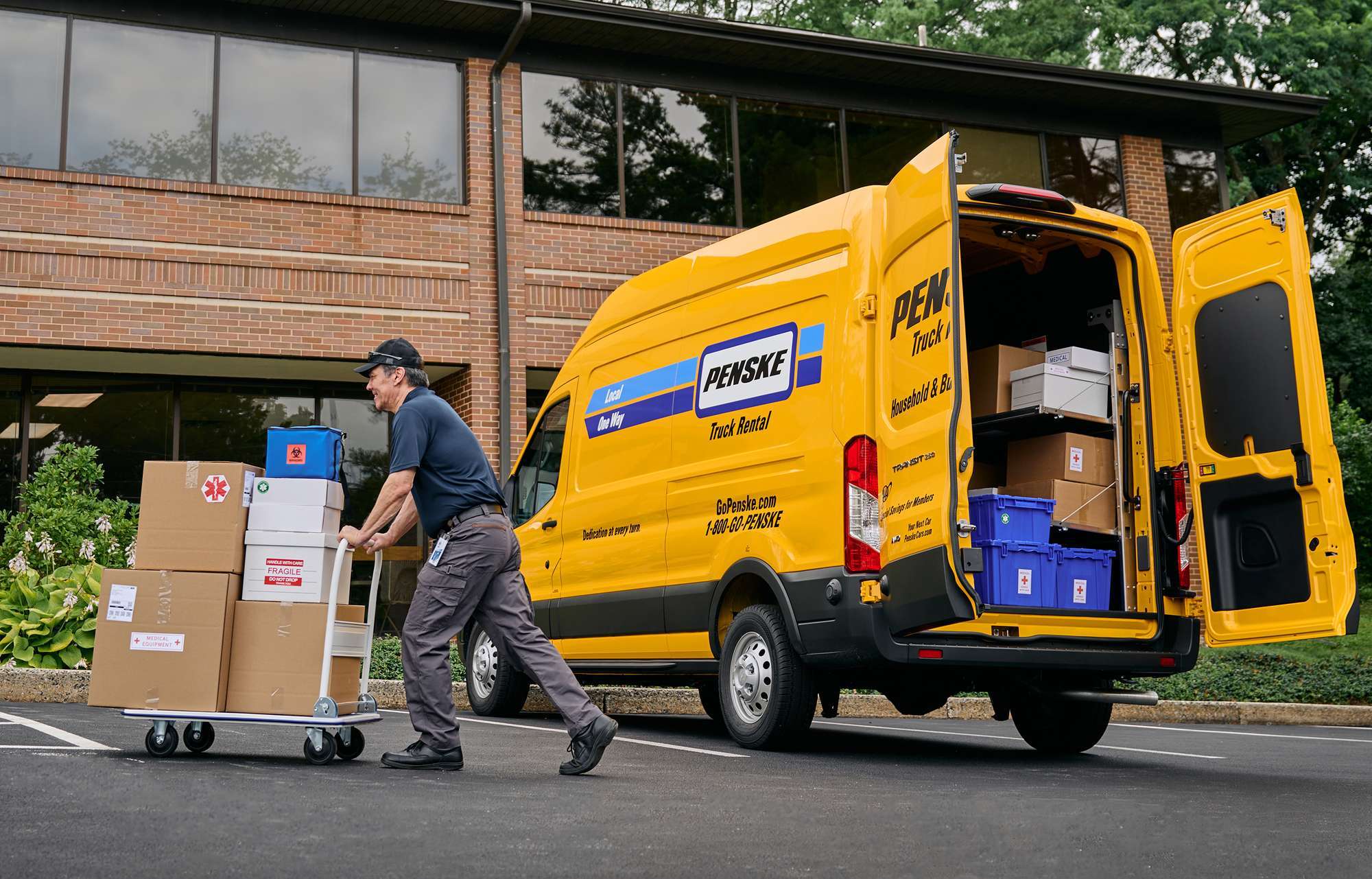 A delivery driver pushes a cart of boxes from a yellow cargo van into a business building.
