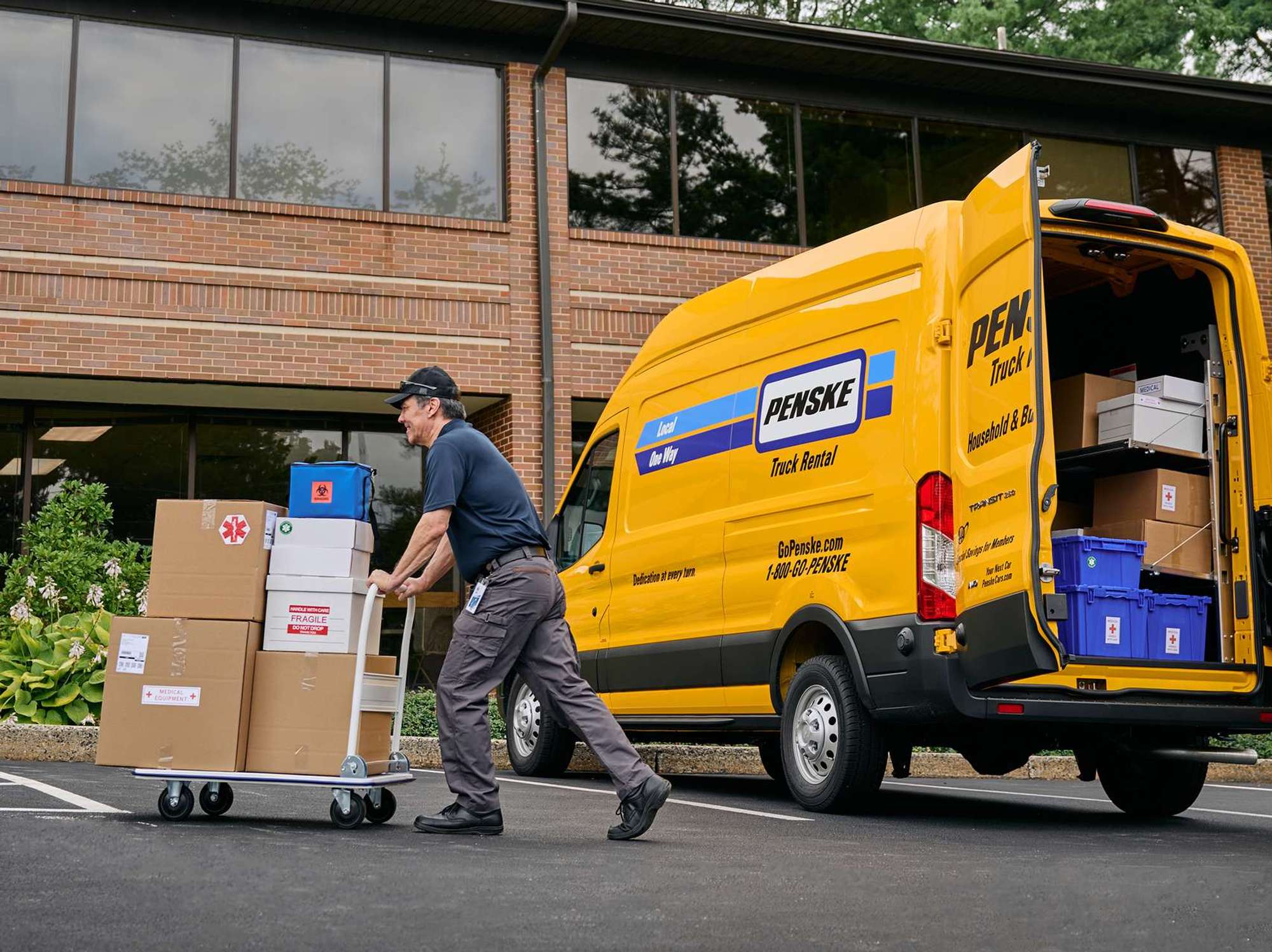 A delivery driver pushes a cart of boxes from a yellow cargo van into a business building.