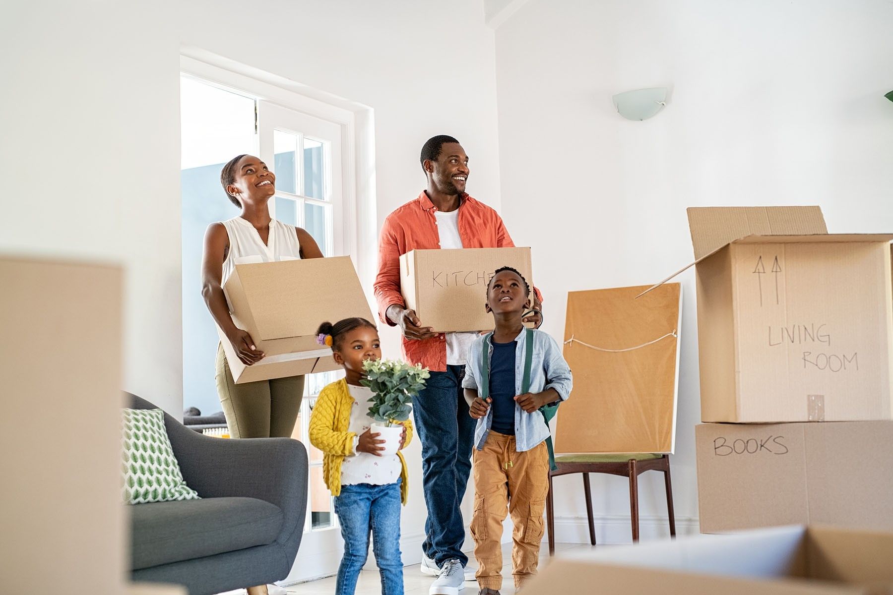 A family with two young kids walks into a new new home carrying boxes and belongings.