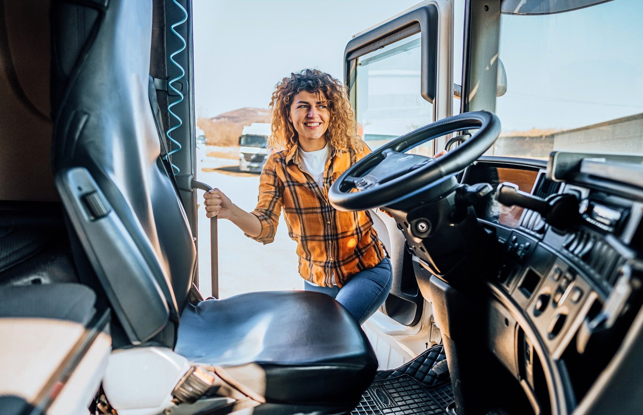 A female truck driver climbs into the cab of a semi truck while holding onto hand rails.