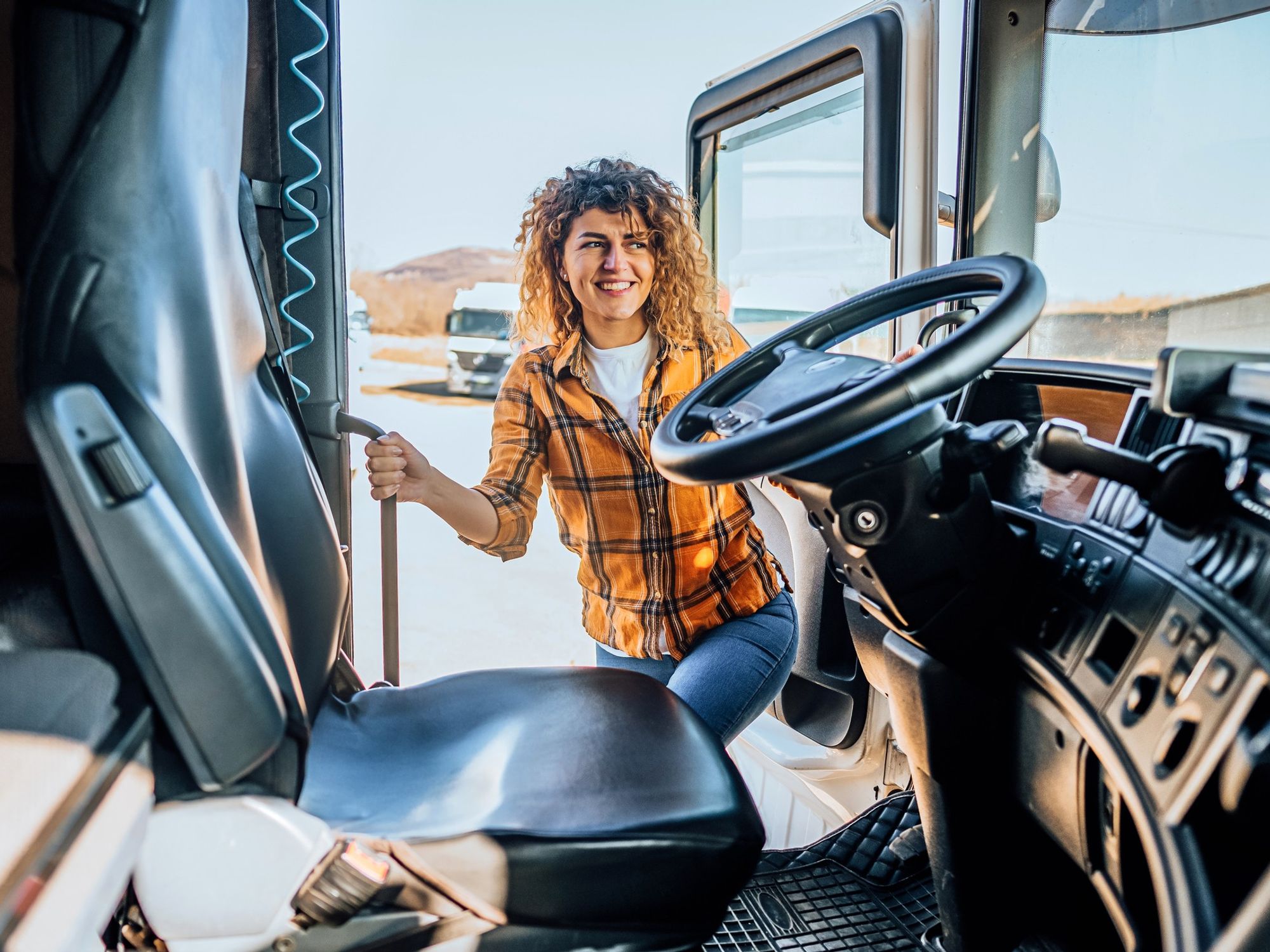 A female truck driver climbs into the cab of a semi truck while holding onto hand rails.
