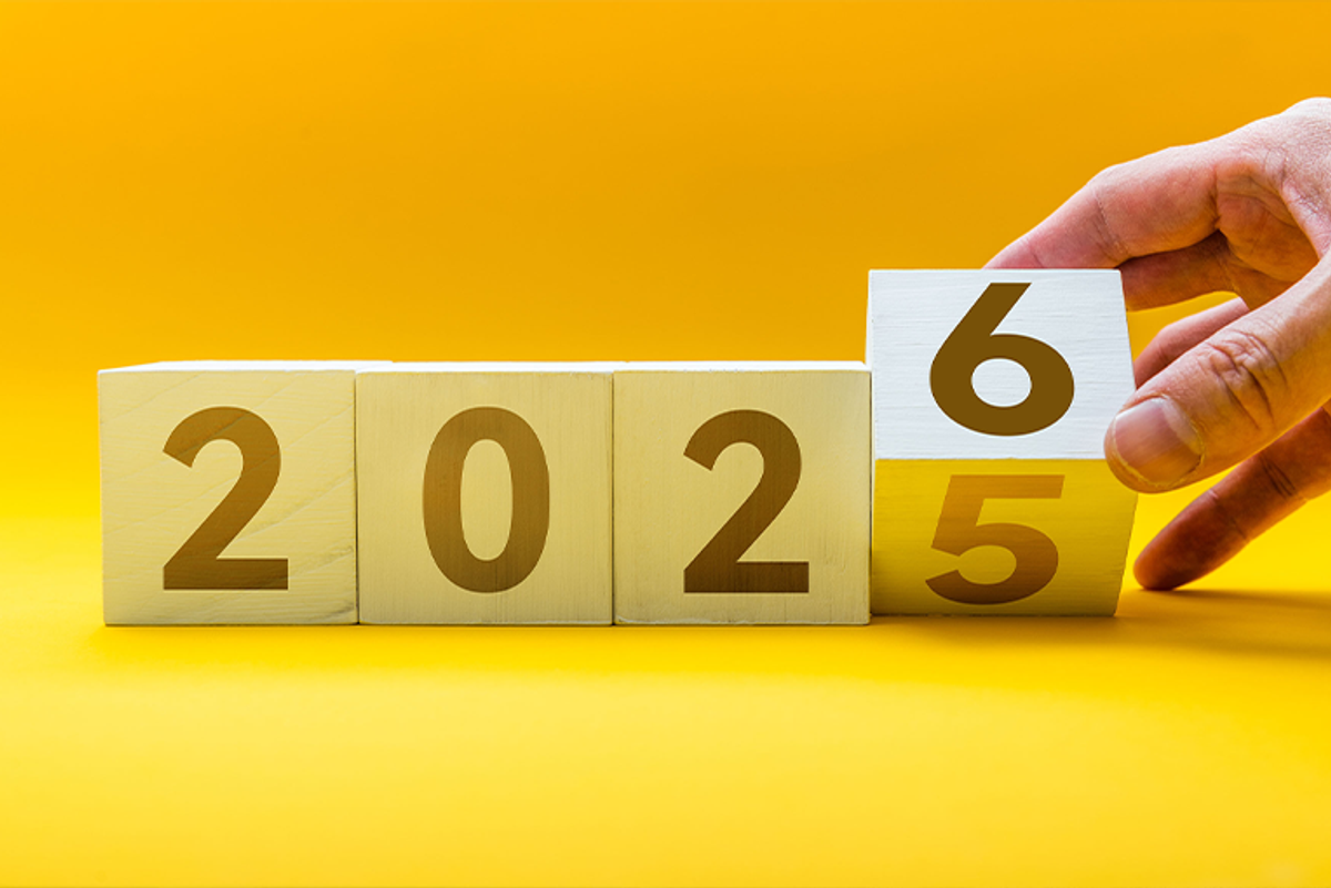 A hand moving blocks from 2025 to 2026 on a yellow background.