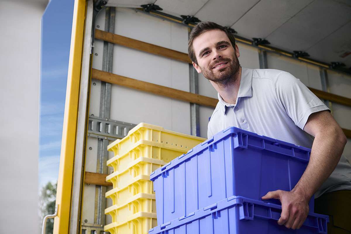 A man holding 2 dark blue containers stands in the back of a rental truck.