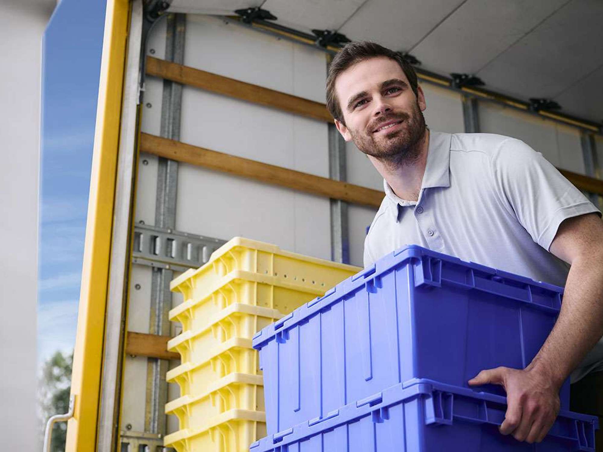 A man holding 2 dark blue containers stands in the back of a rental truck.