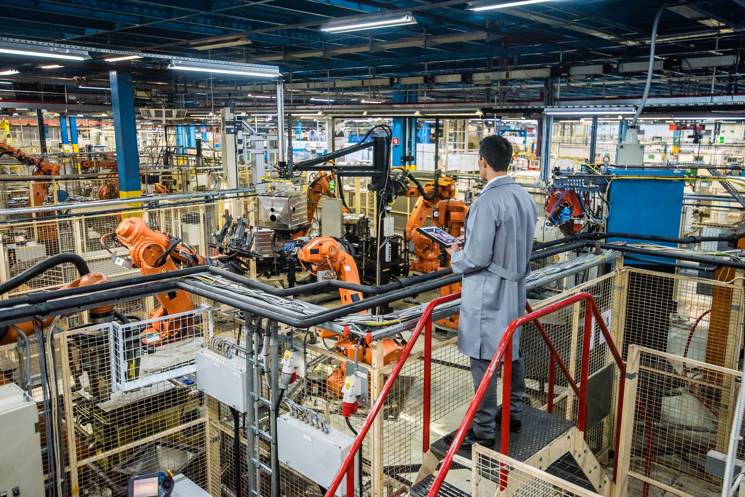 A man holding a tablet looks out over a manufacturing warehouse.