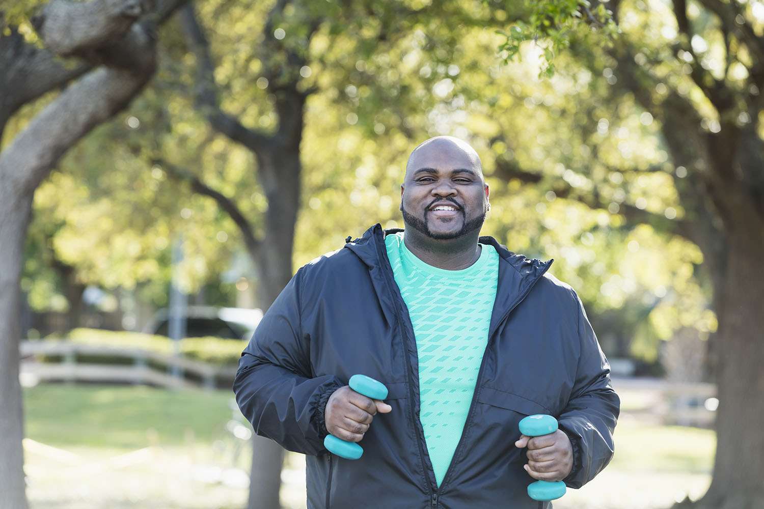 A man in a t-shirt and light jacket walks with blue handweights in his hands.