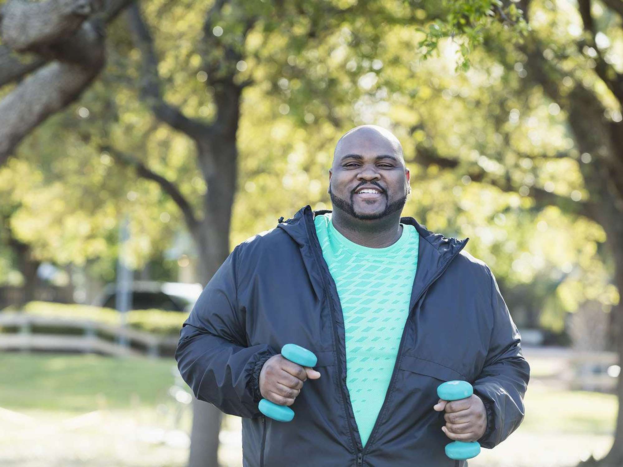 A man in a t-shirt and light jacket walks with blue handweights in his hands.