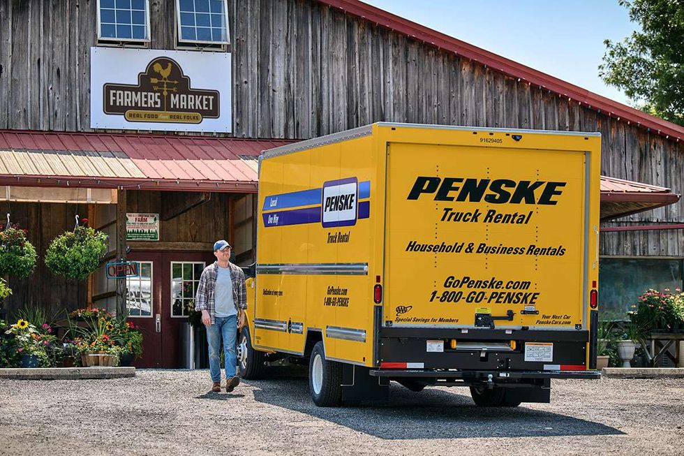 A man walks out of a farmer's market next to a yellow Penske box truck.