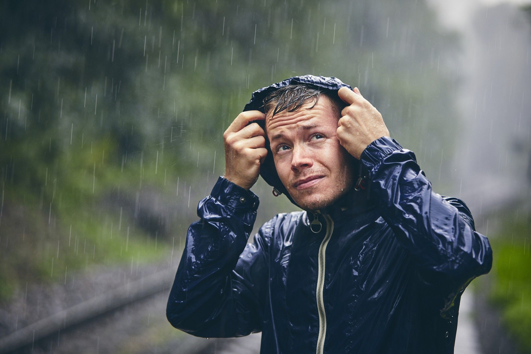A man with a blue rain jacket stands outside in a rain downpour.