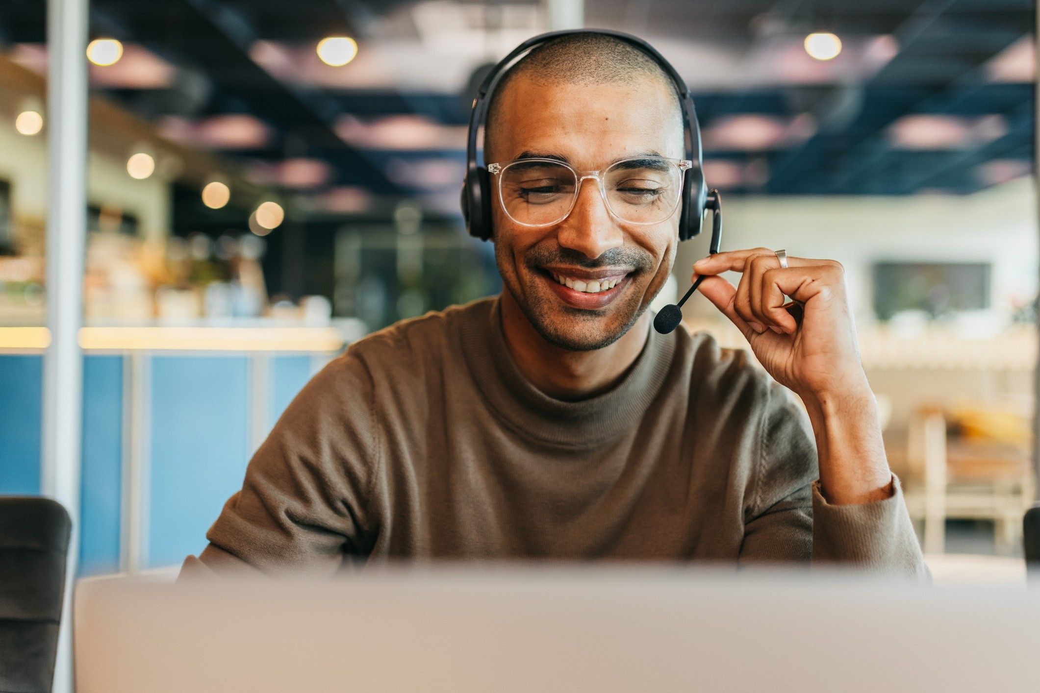 A man with a headset sits at a desk smiling.