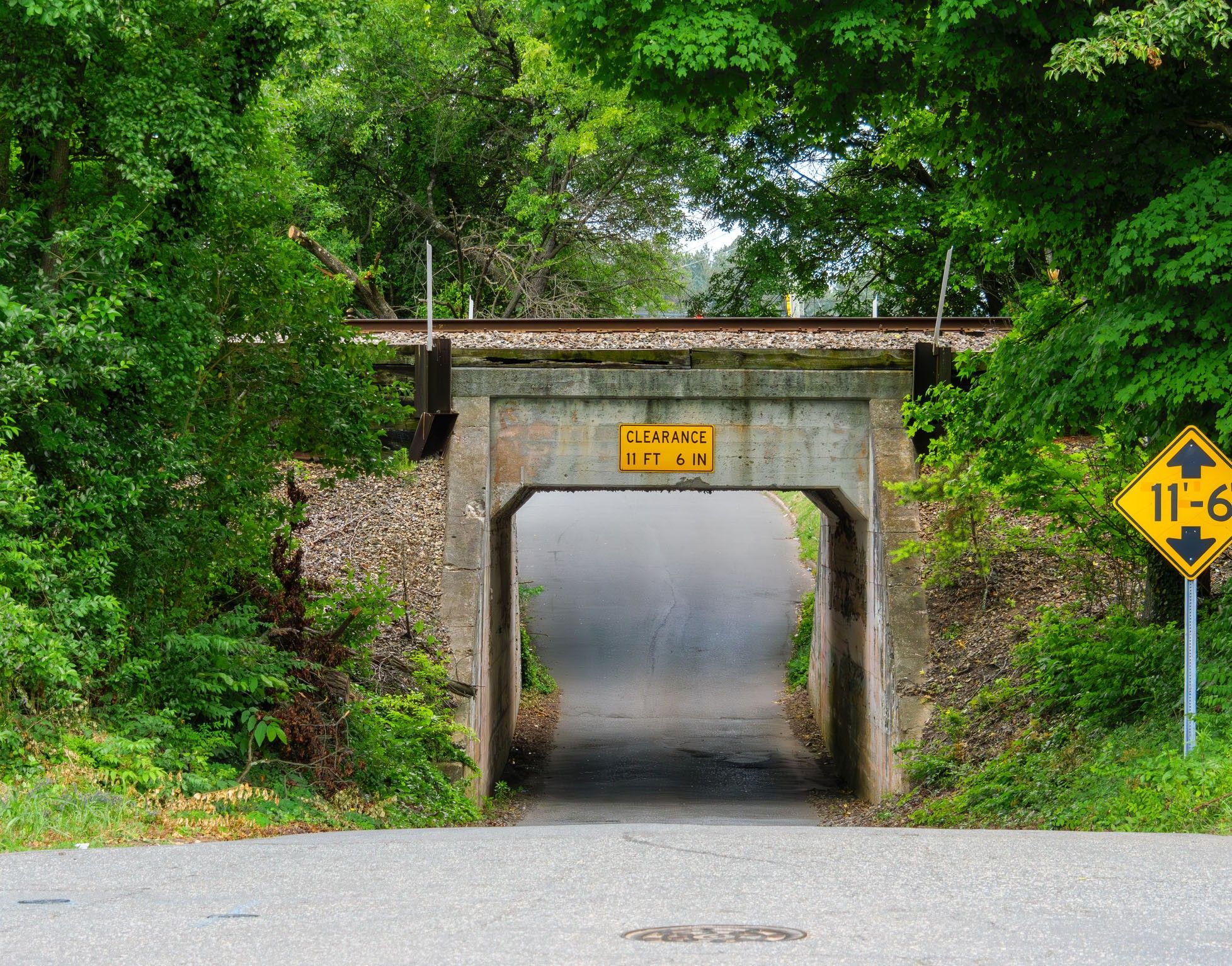 A narrow cement bridge with a 11 ft 6 in low clearance sign and a railroad track on top.