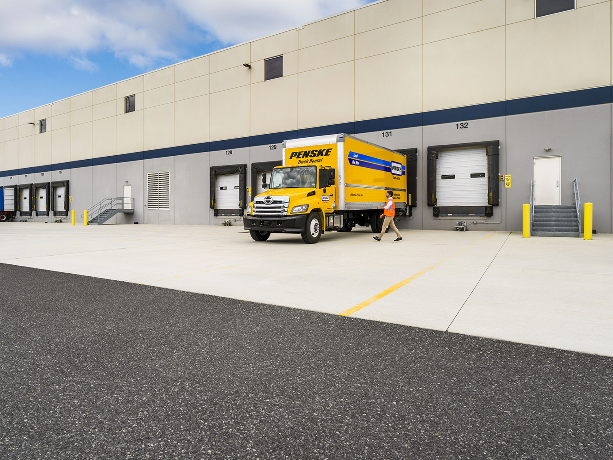 A person walks towards a yellow Penske truck parked at a loading dock.