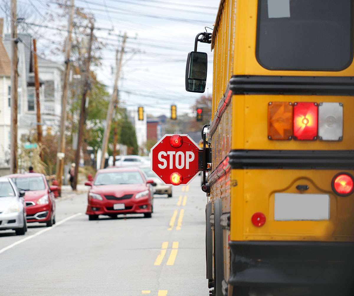 A school bus stopped on the road with it's stop sign out and flashing.
