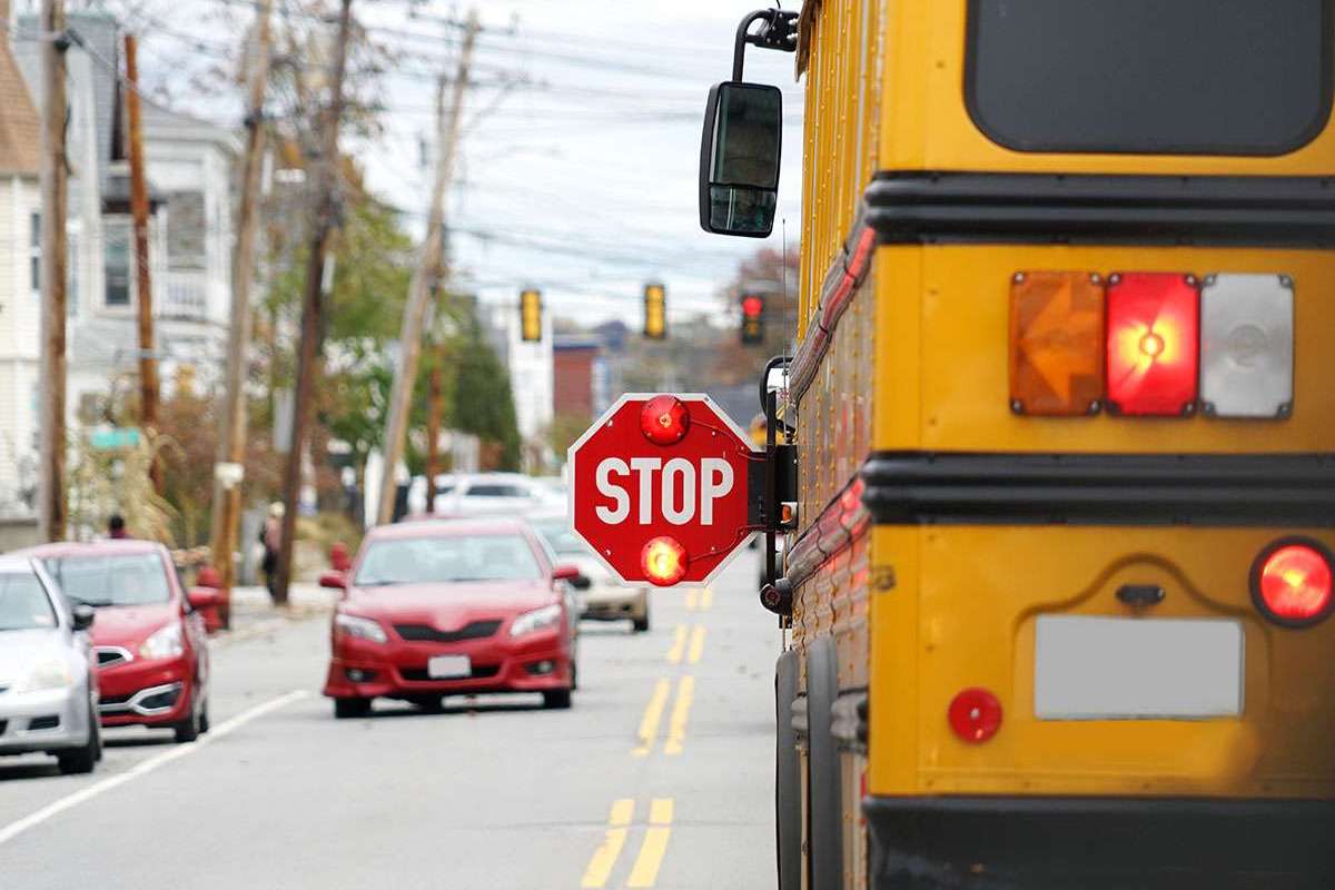 A school bus stopped on the road with it's stop sign out and flashing.