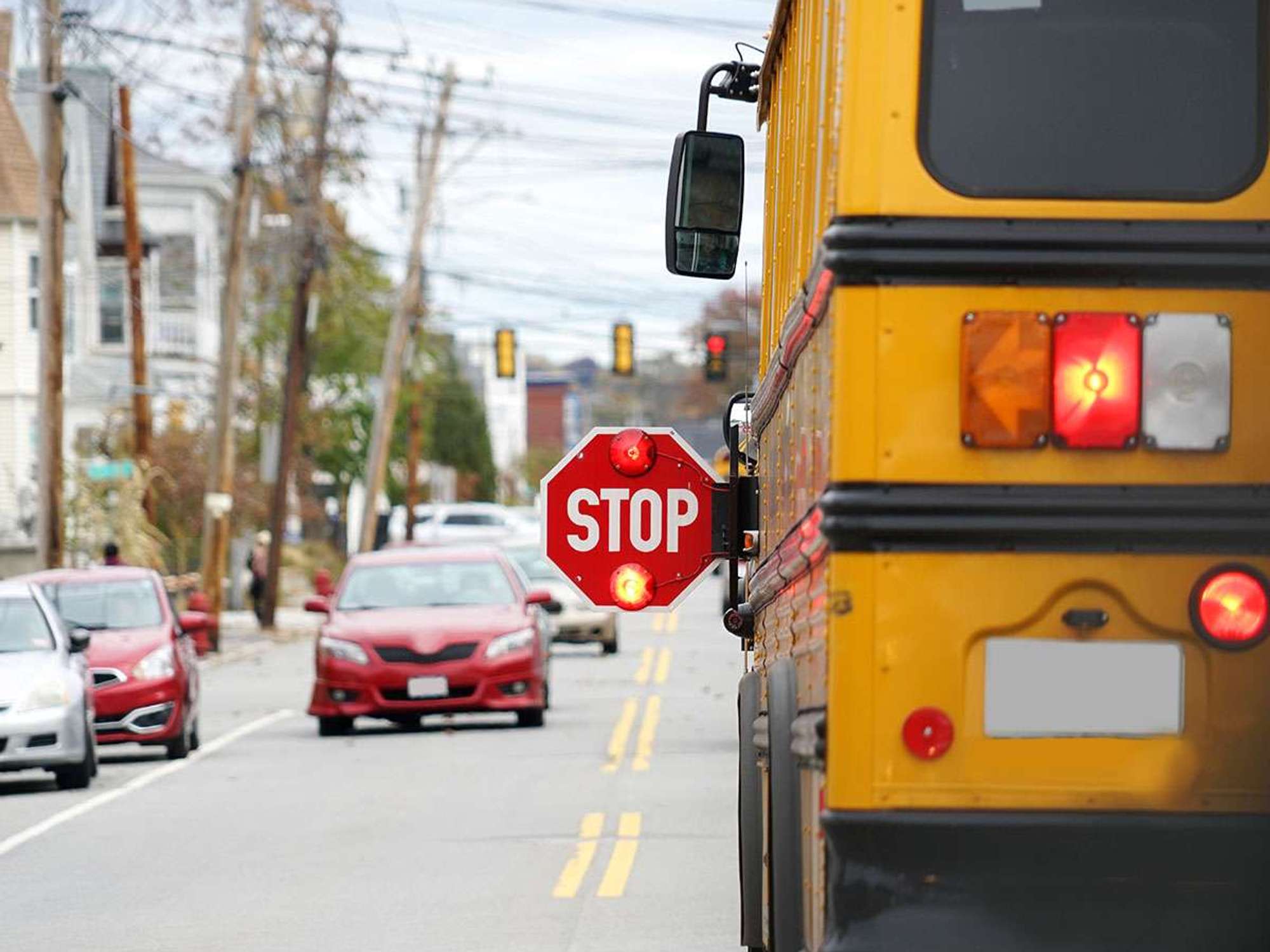 A school bus stopped on the road with it's stop sign out and flashing.