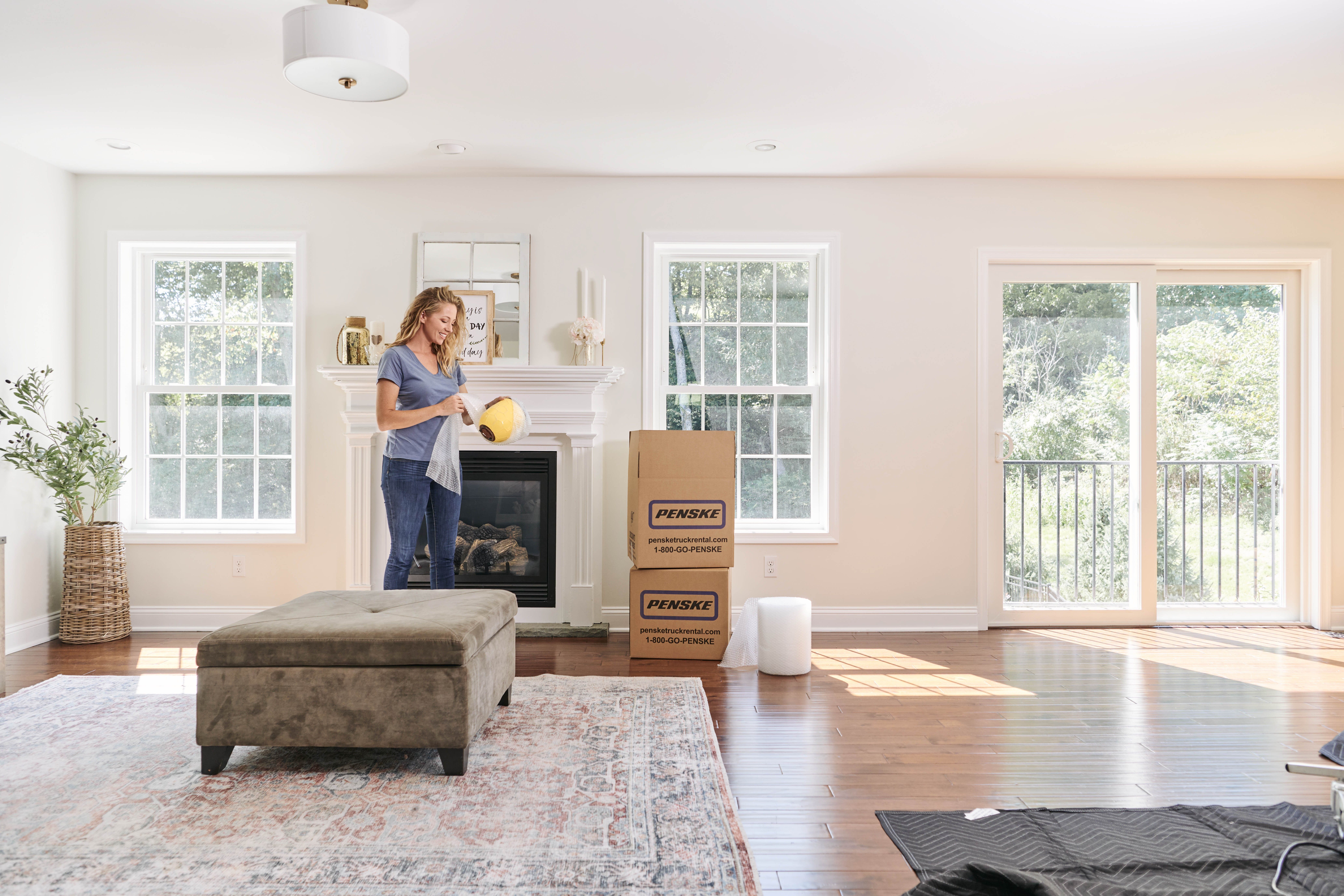A woman in her living room wraps a vase in bubble wrap to pack.
