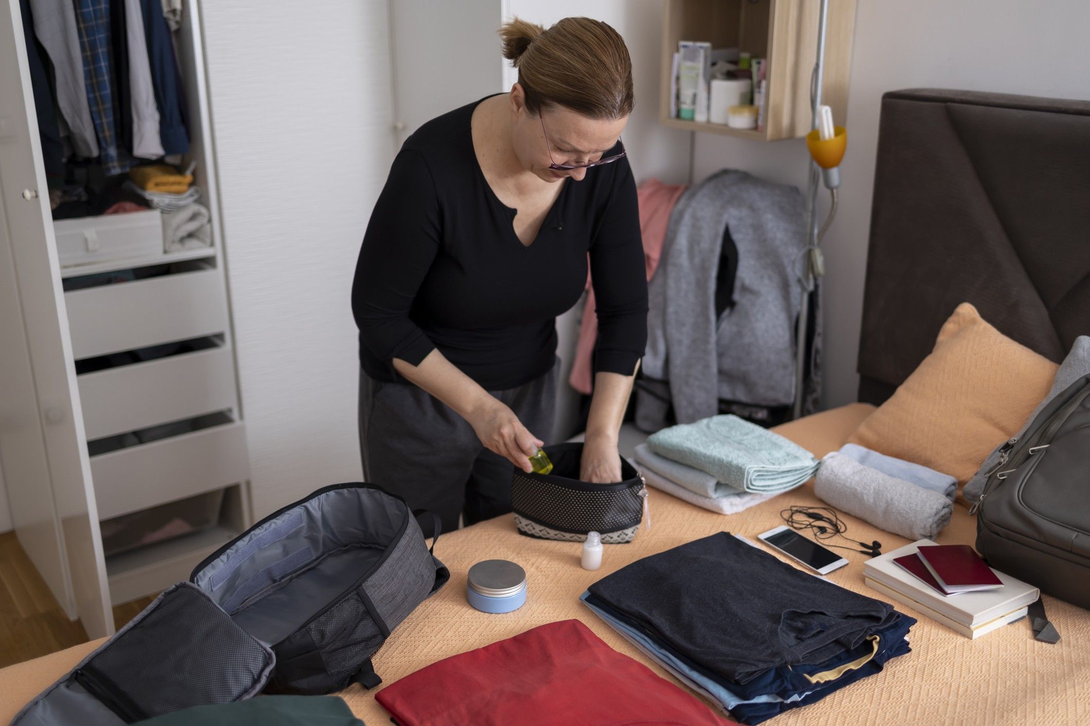 A woman packs items into a small suitcase.