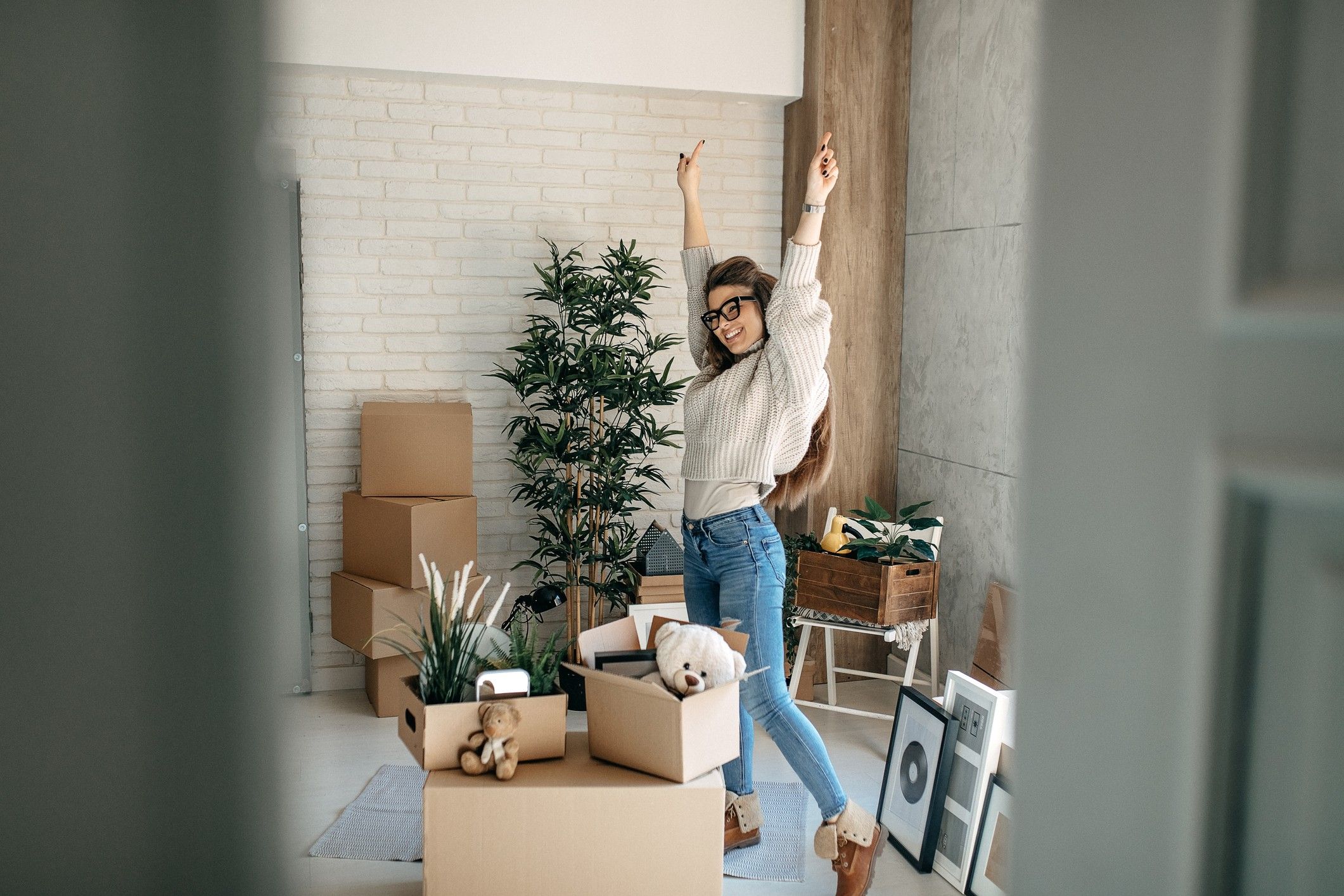 A woman raises her arms in excitement as she unpacks boxes in a new apartment.