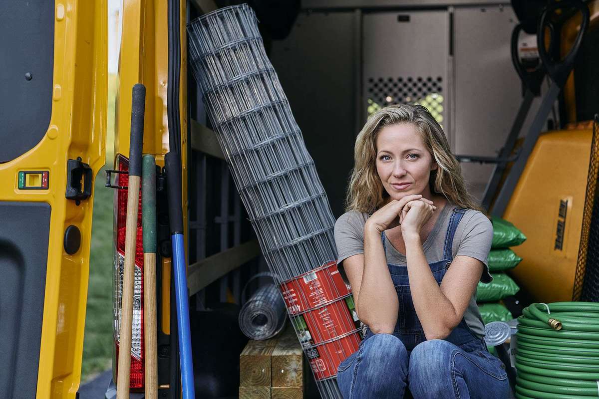 A woman sits in the back of a yellow Penske truck surrounded by tools and fencing.
