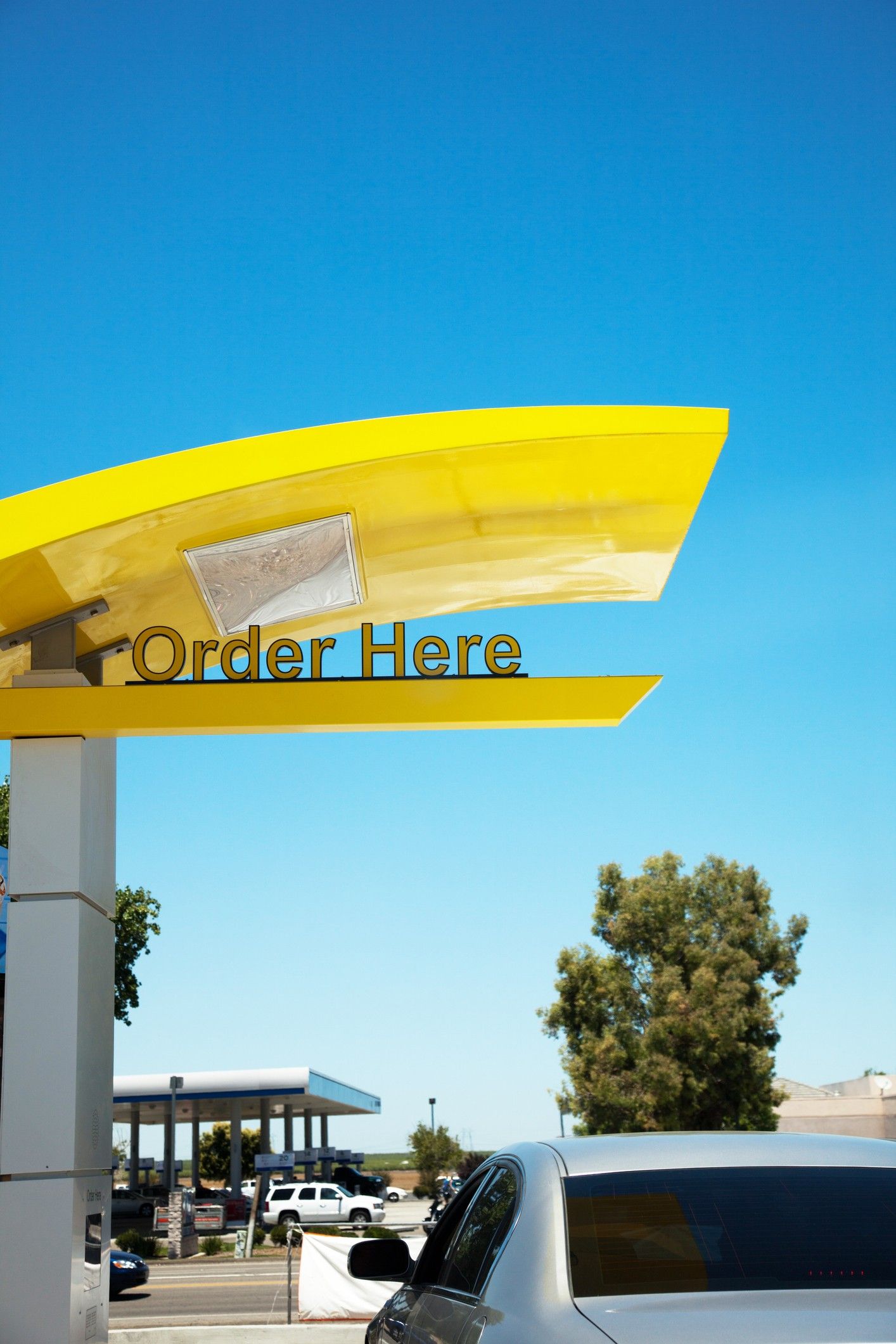 A yellow Order Here awning and sign at a fast food drive thru.