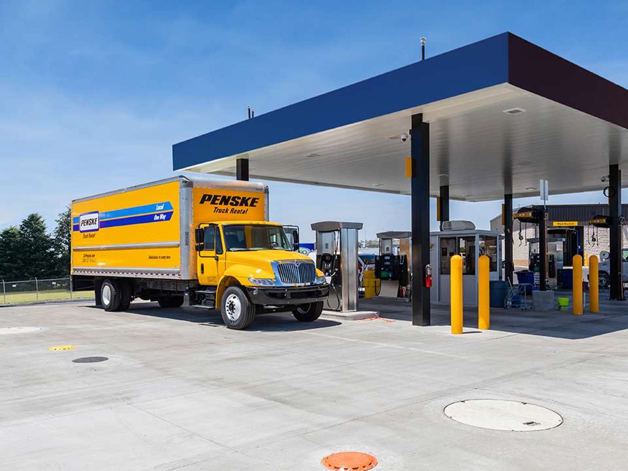 A yellow Pensk truck is parked at a fuel pump.