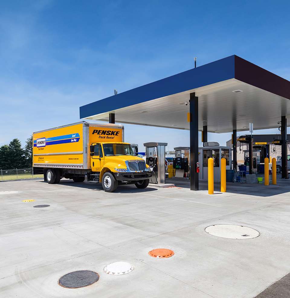 A yellow Pensk truck is parked at a fuel pump.