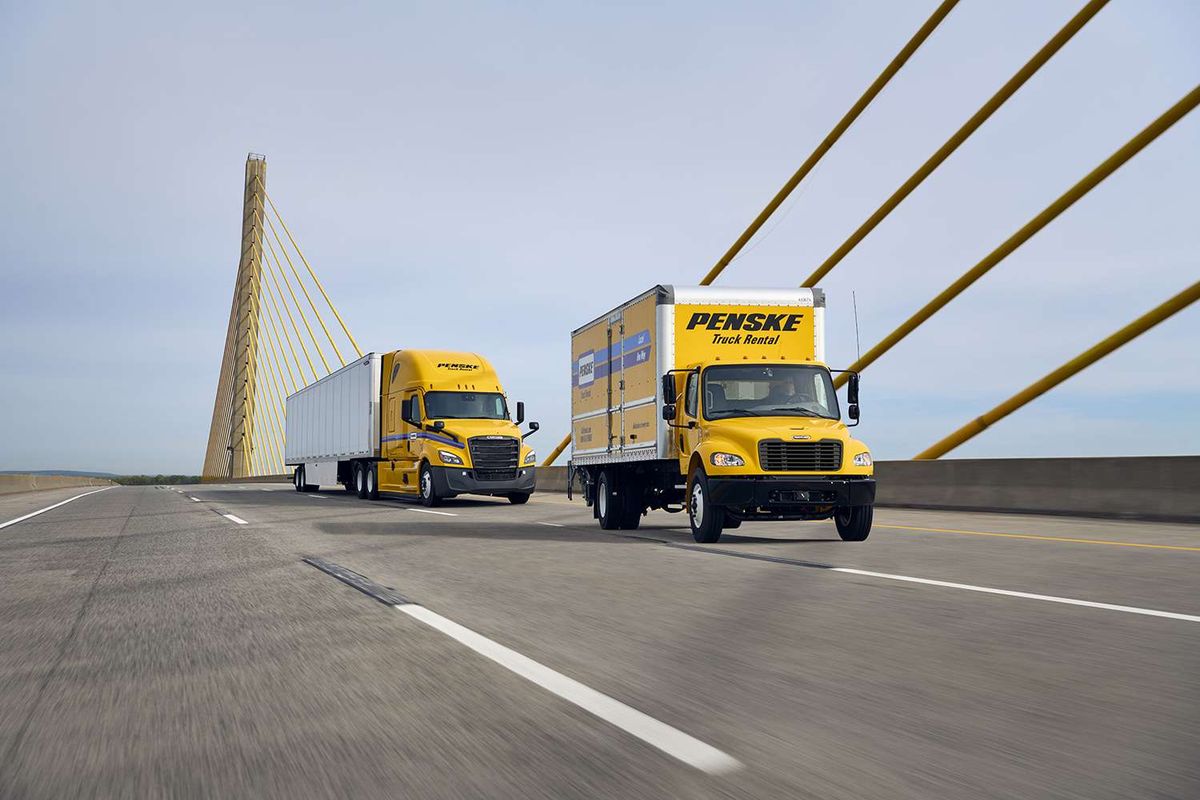 A yellow Penske box truck and yellow Penske semi-truck drive across a bridge.