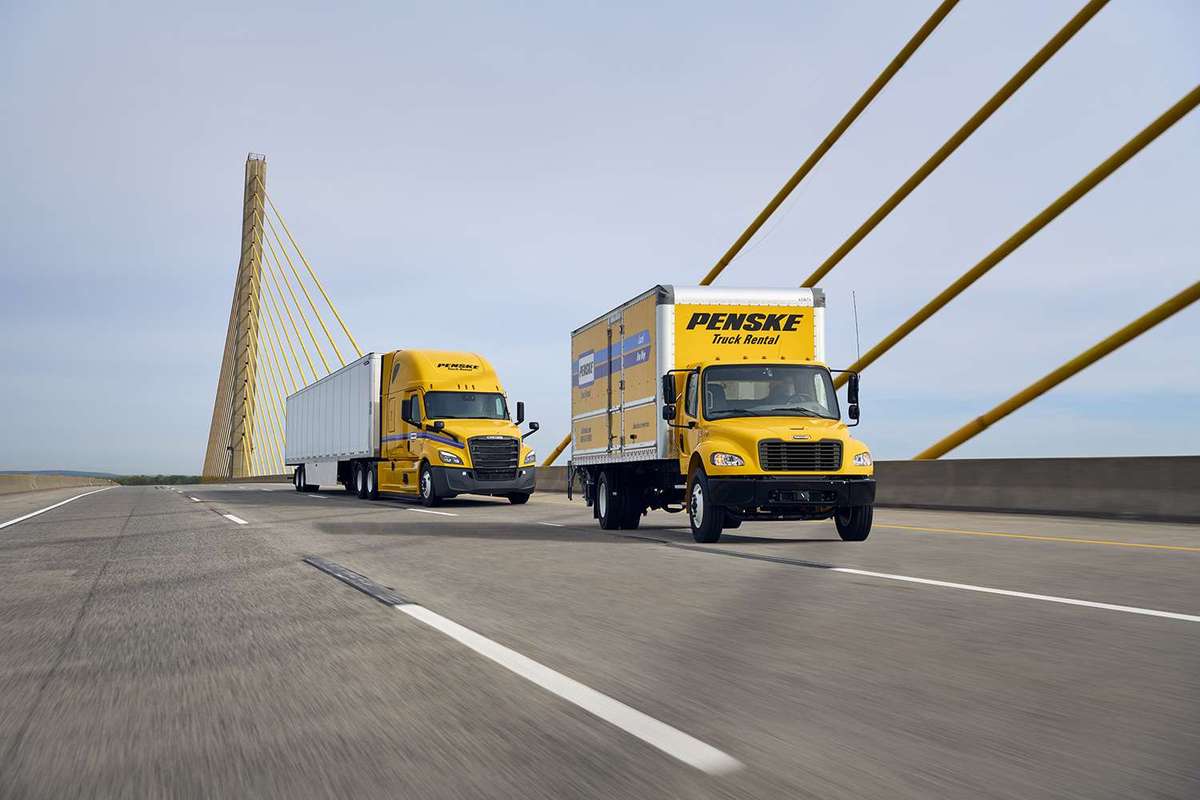 A yellow Penske box truck and yellow Penske semi-truck drive across a bridge.