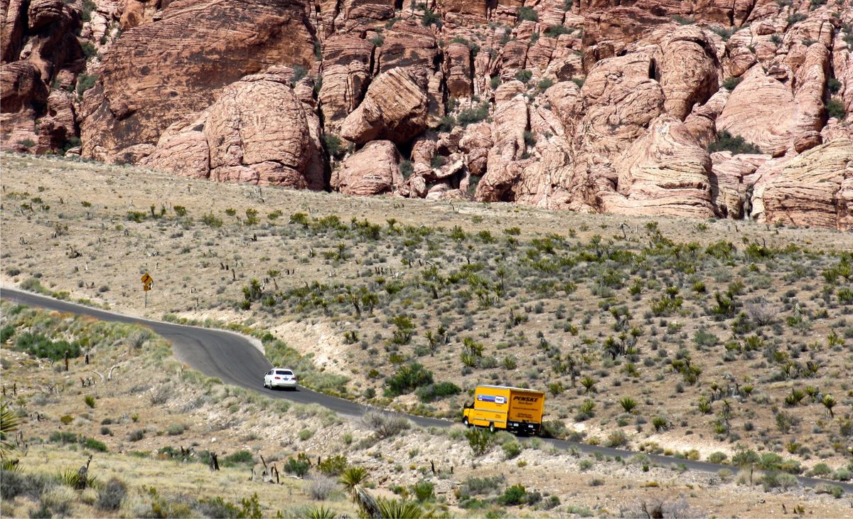 A yellow Penske box truck drives on a road through the desert.
