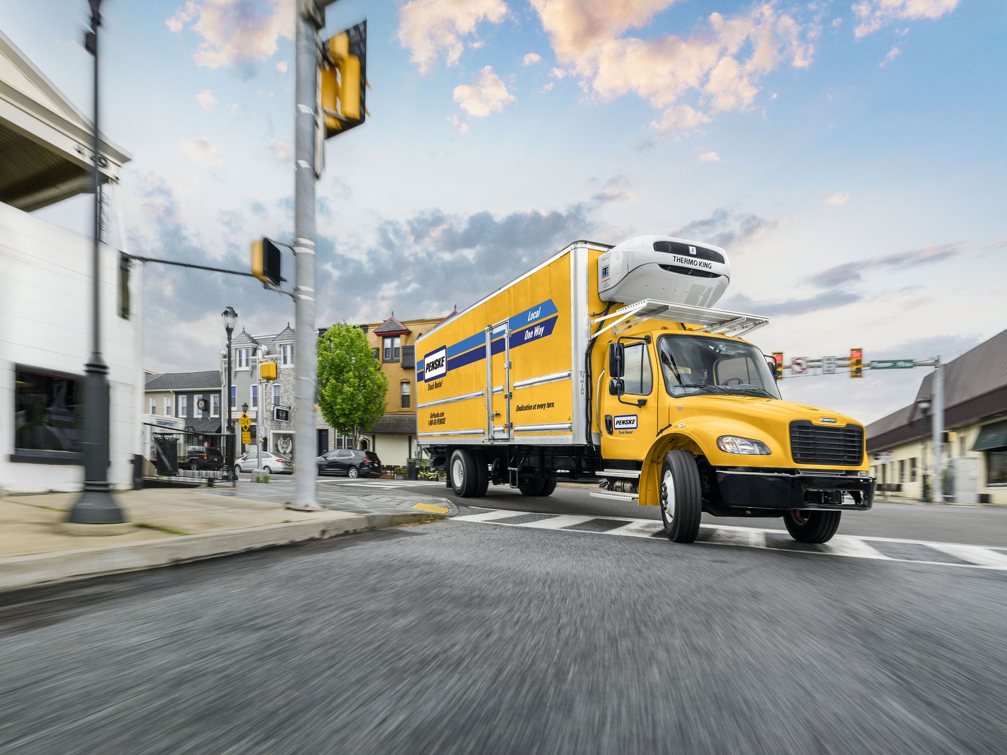 A yellow Penske refrigerated box truck driving on a road at sunset.