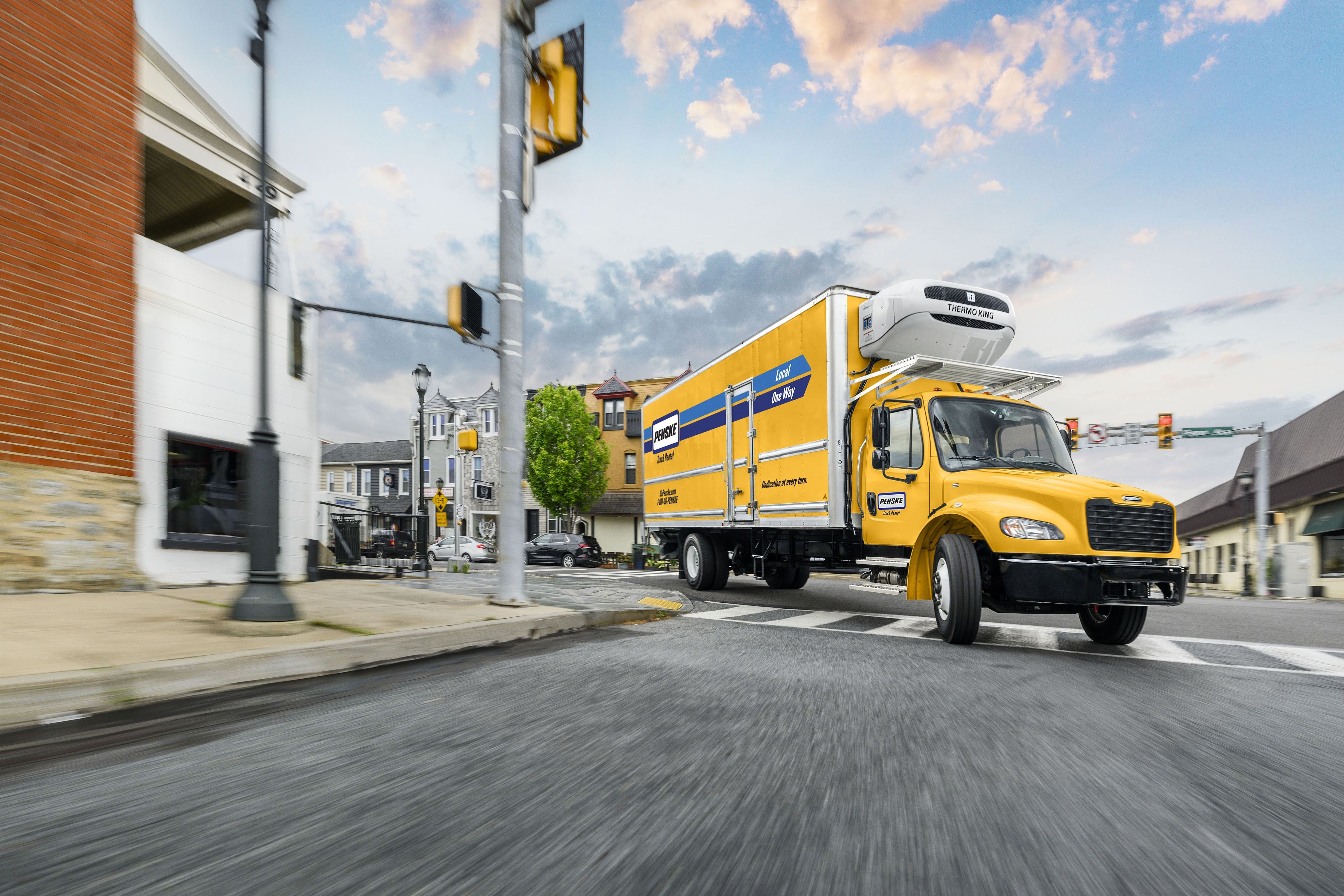 A yellow Penske refrigerated box truck driving on a road at sunset.