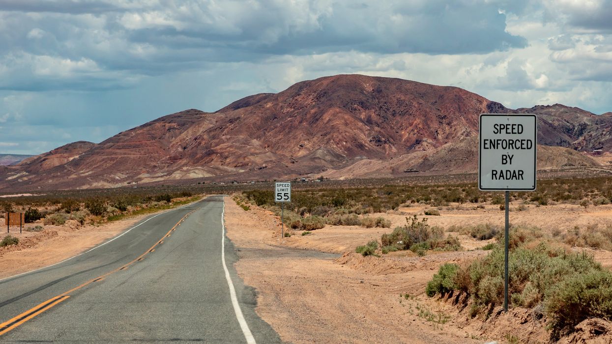 An empty desert road with a Speed Enforced By Radar sign.