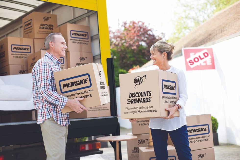 An older man and woman carry Penske moving boxes out of a Penske moving truck.