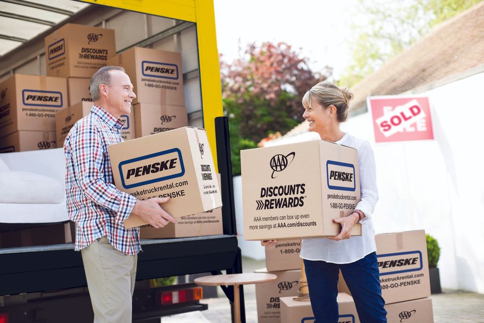 An older man and woman carry Penske moving boxes out of a Penske moving truck.