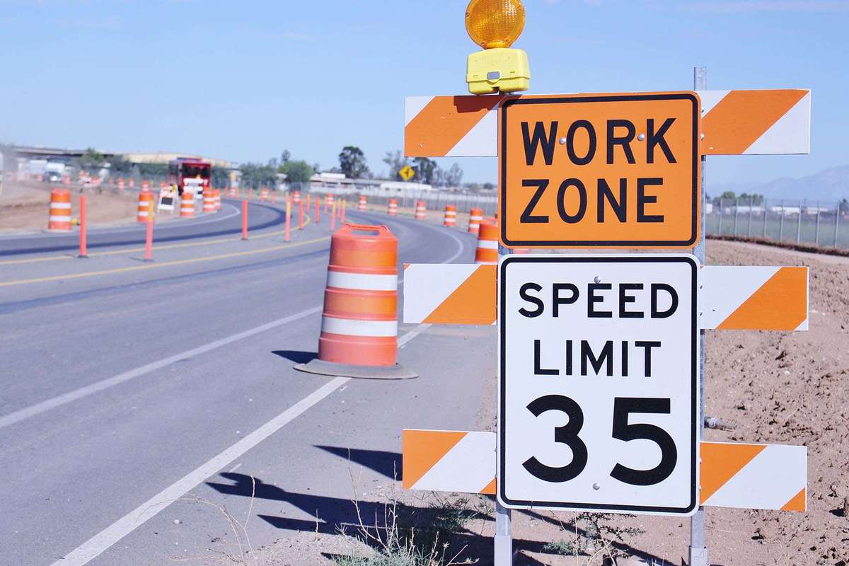 An orange work zone sign and speed limit 35 sign next to a road filled with orange construction barrels.