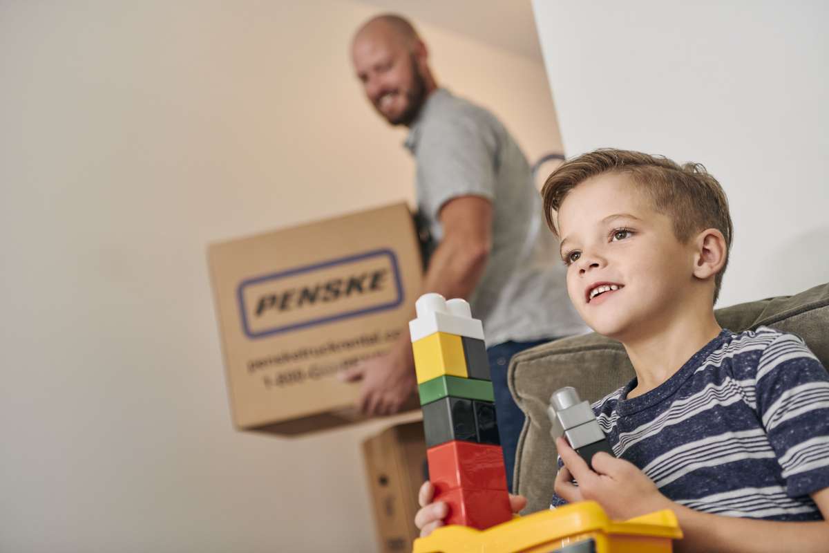 Boy plays with legos, dad moves boxes.