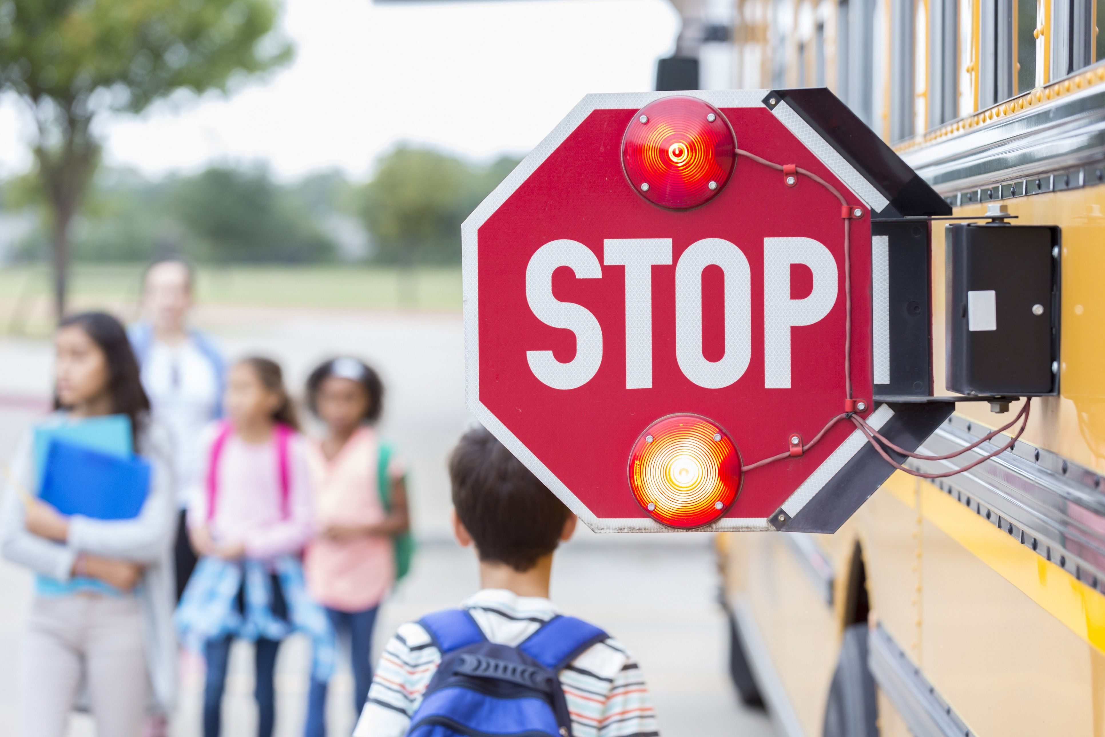 Closeup of the pop-out stop sign on the side of a school bus with kids walking by.