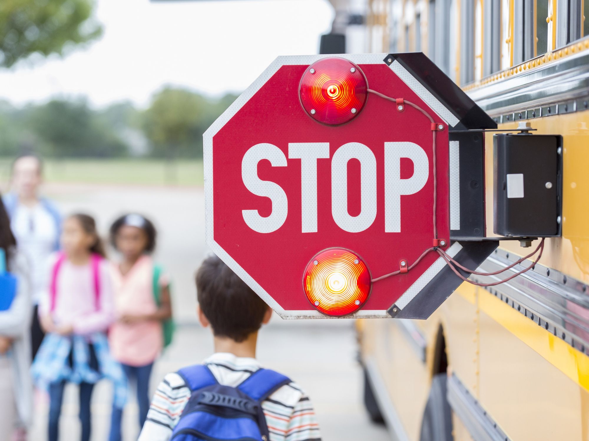 Closeup of the pop-out stop sign on the side of a school bus with kids walking by.