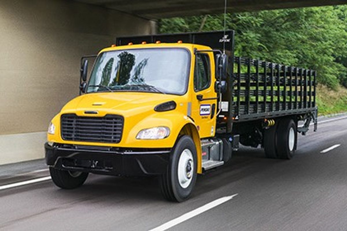 Penske flatbed truck (non-CDL) on a highway passing under a bridge