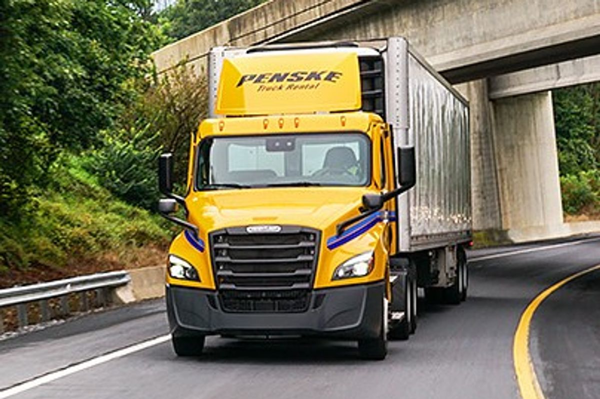 Penske tandem-axle day cab tractor on a highway passing under a bridge