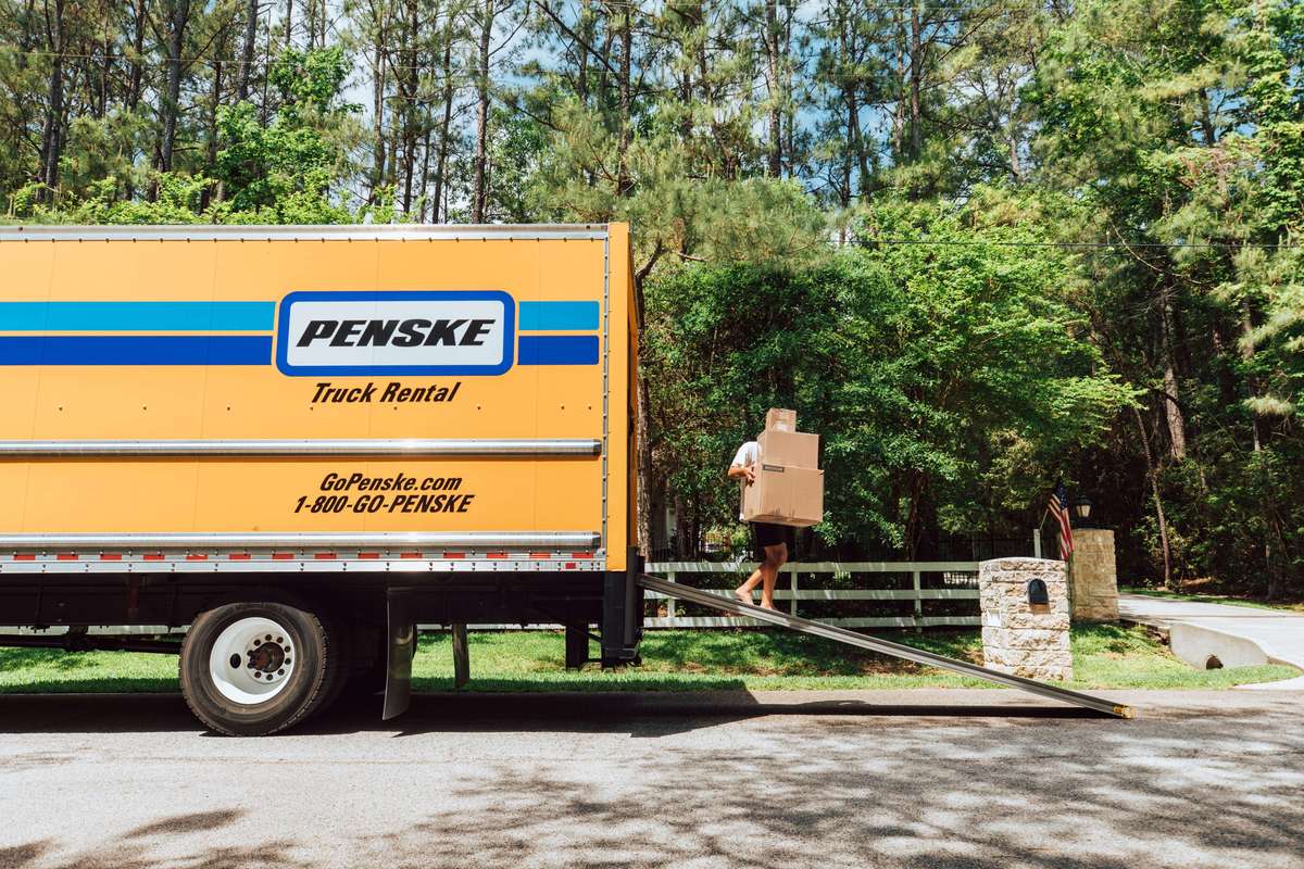 Person unloading boxes from a Penske truck on a sunny day.