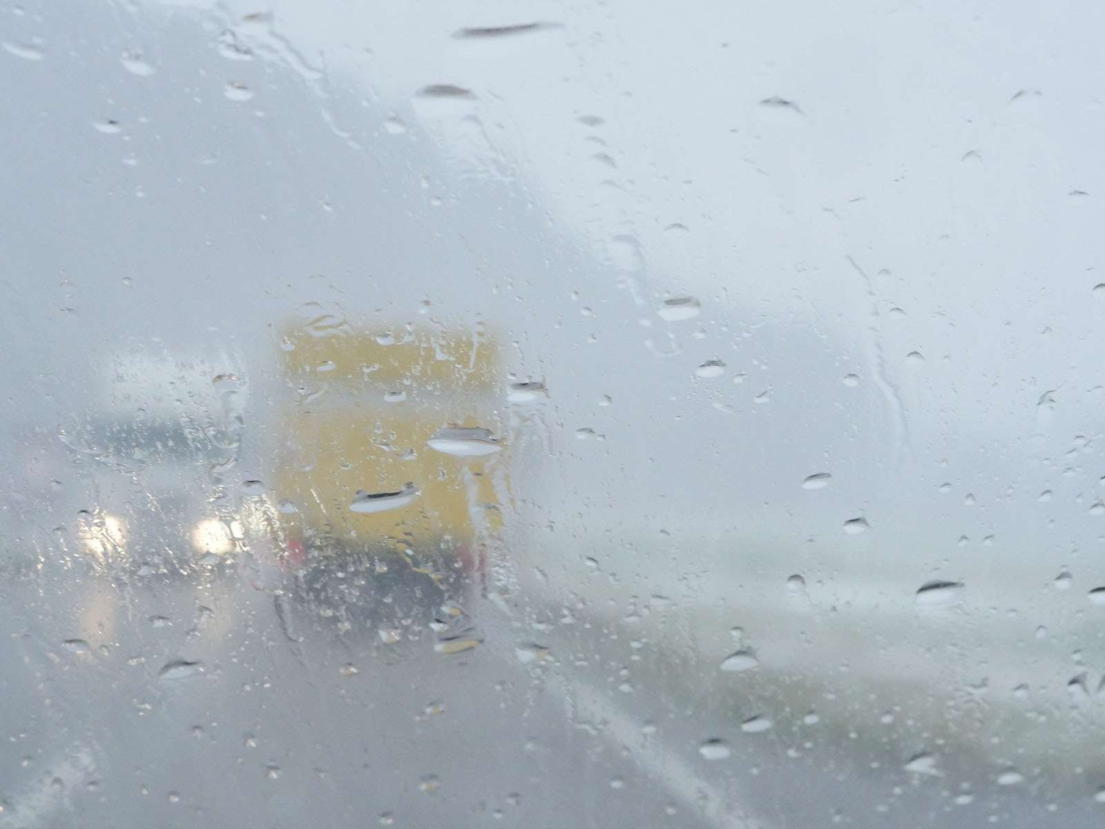 The back of a yellow box truck through a rainy windshield
