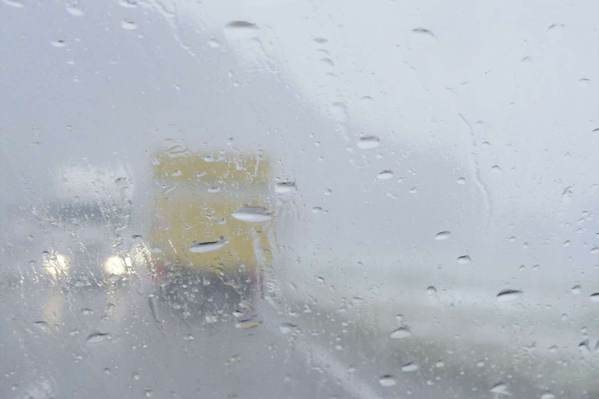 The back of a yellow box truck through a rainy windshield