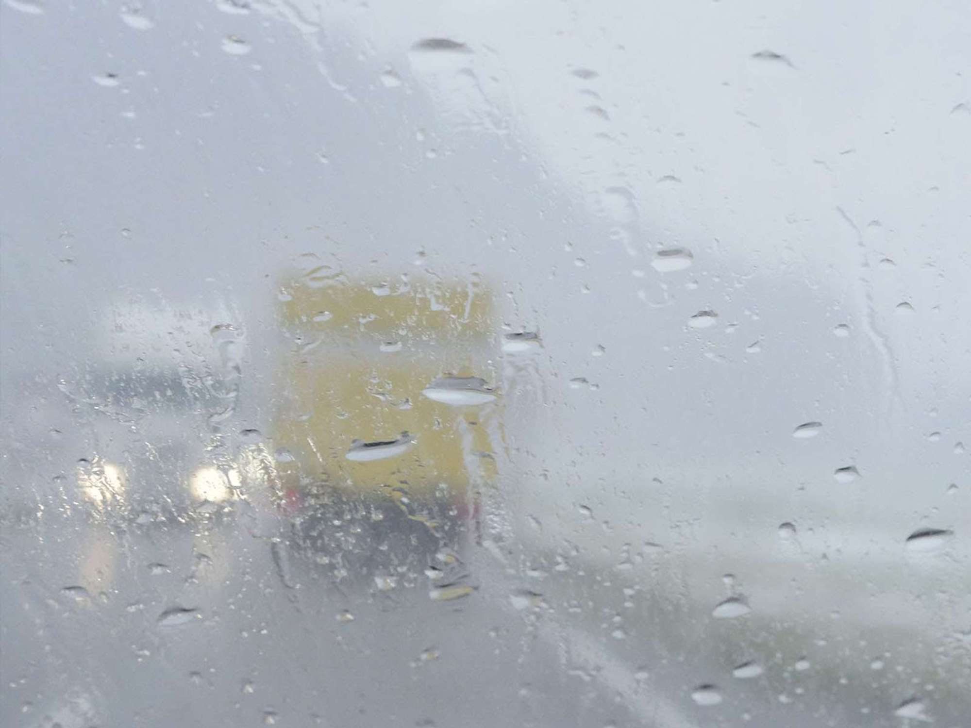 The back of a yellow box truck through a rainy windshield