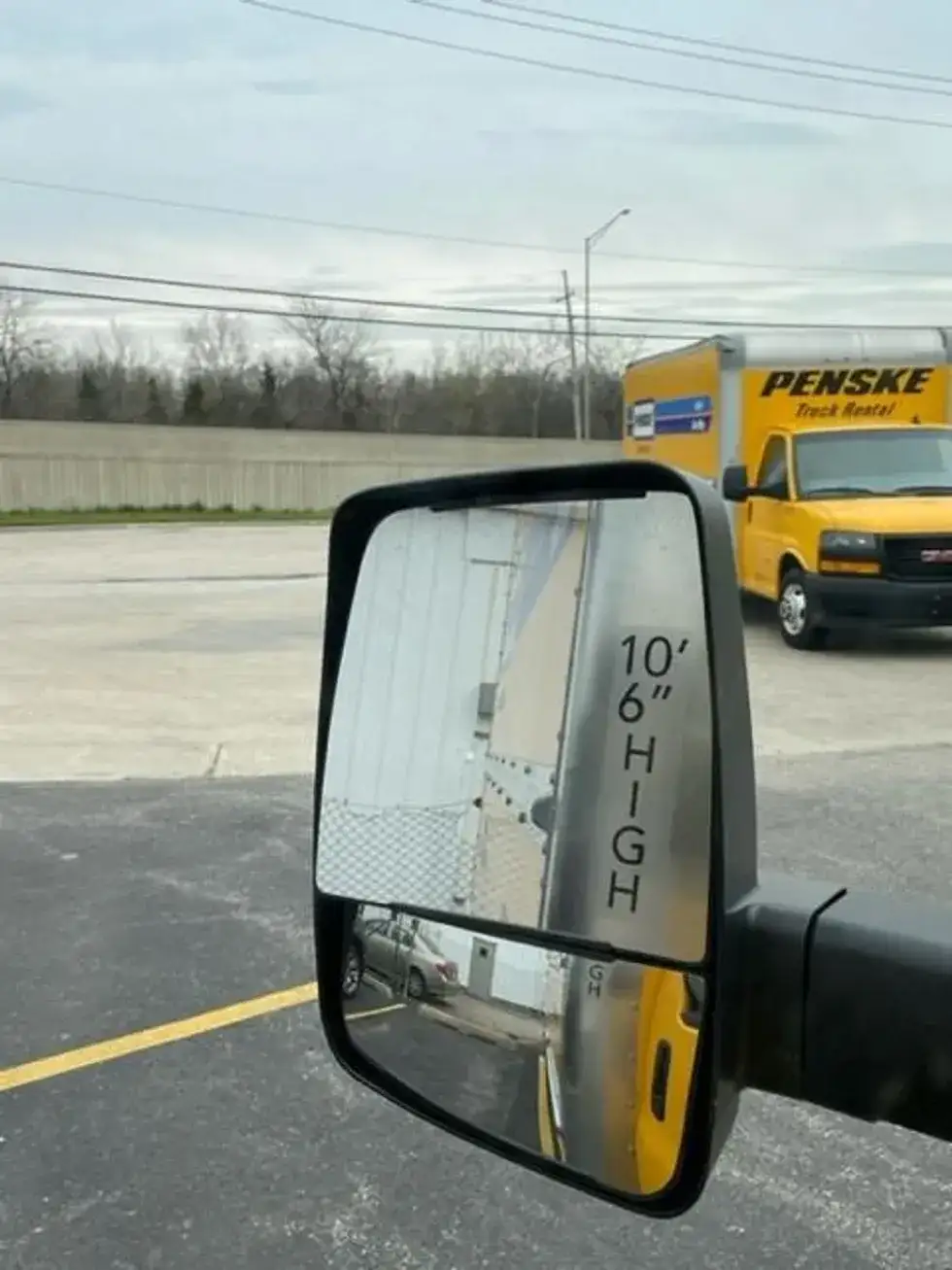 The driver's side mirror of a penske truck reflecting the 10' 6" clearance of the truck.