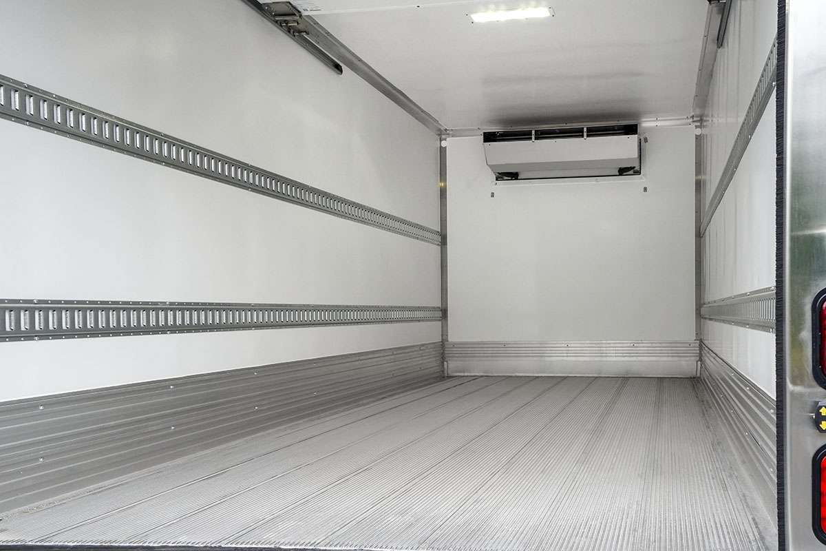 The inside back of an empty Penske box truck with grey floors, white walls, and metal e-track rails.