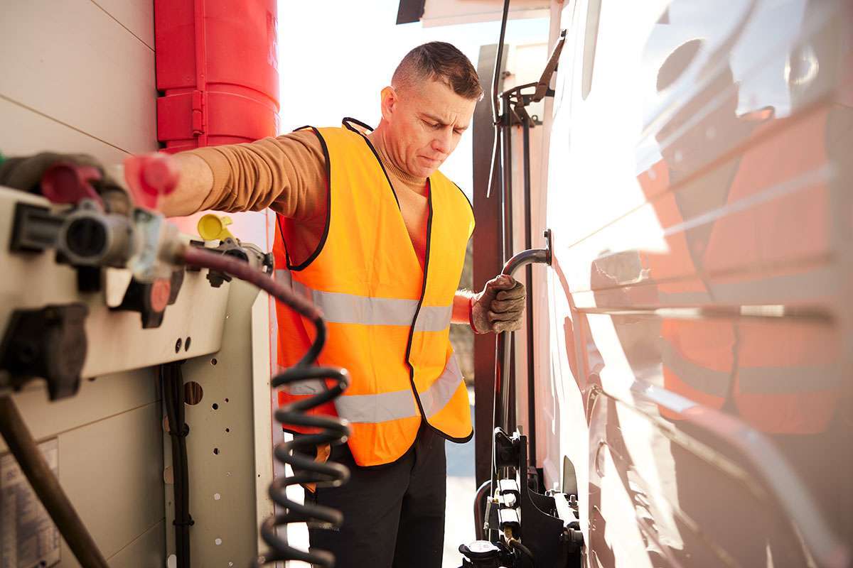 Truck driver in an orange vest and gloves examining semi-truck trailer brake coil for safety